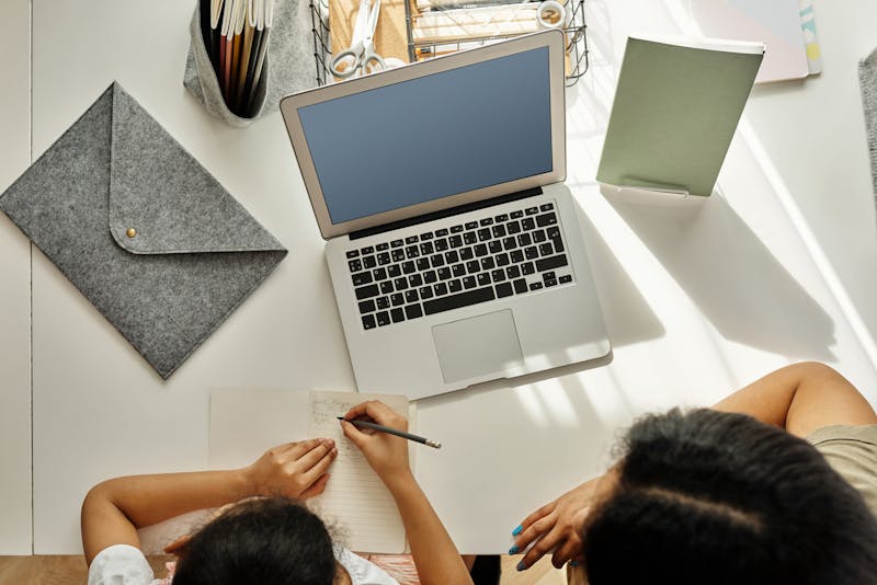 Mother helping her daughter with maths homework at a desk, working through problems together